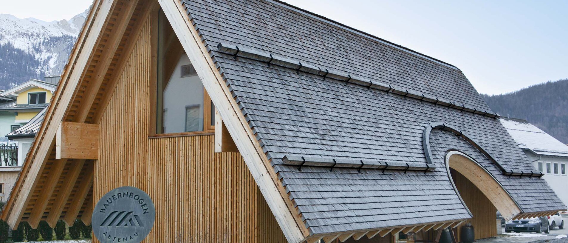 Bauernbogen Abtenau – Architekturansicht mit geschwungenem Dach und vertikaler Holzfassade, umgesetzt mit LIGNOLOC® Holznägeln von BECK
