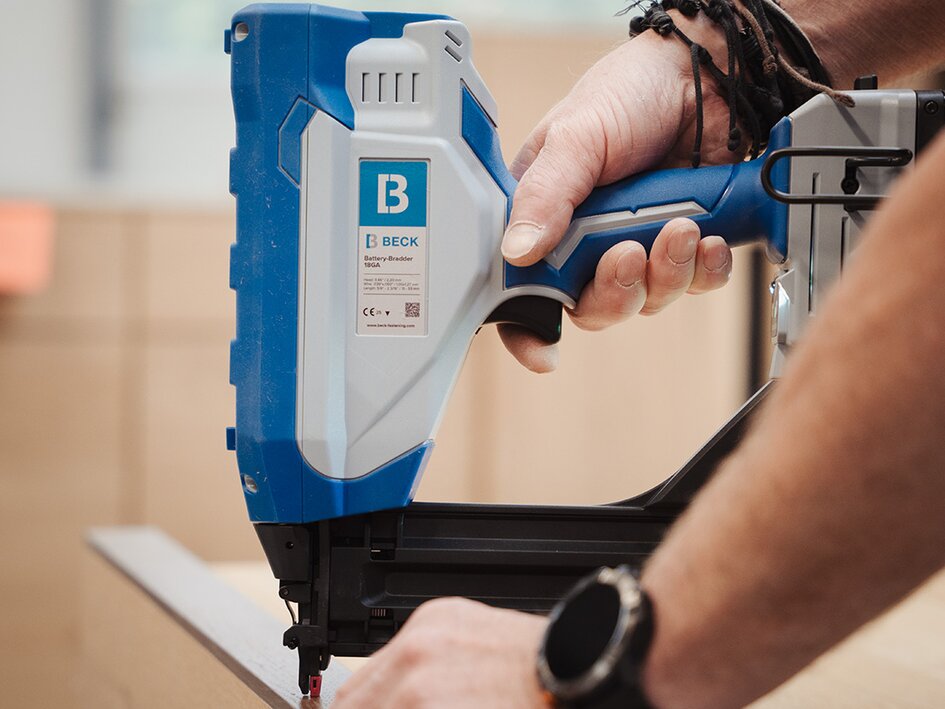 Craftsman using a BECK battery-powered brad nailer on a wooden surface.