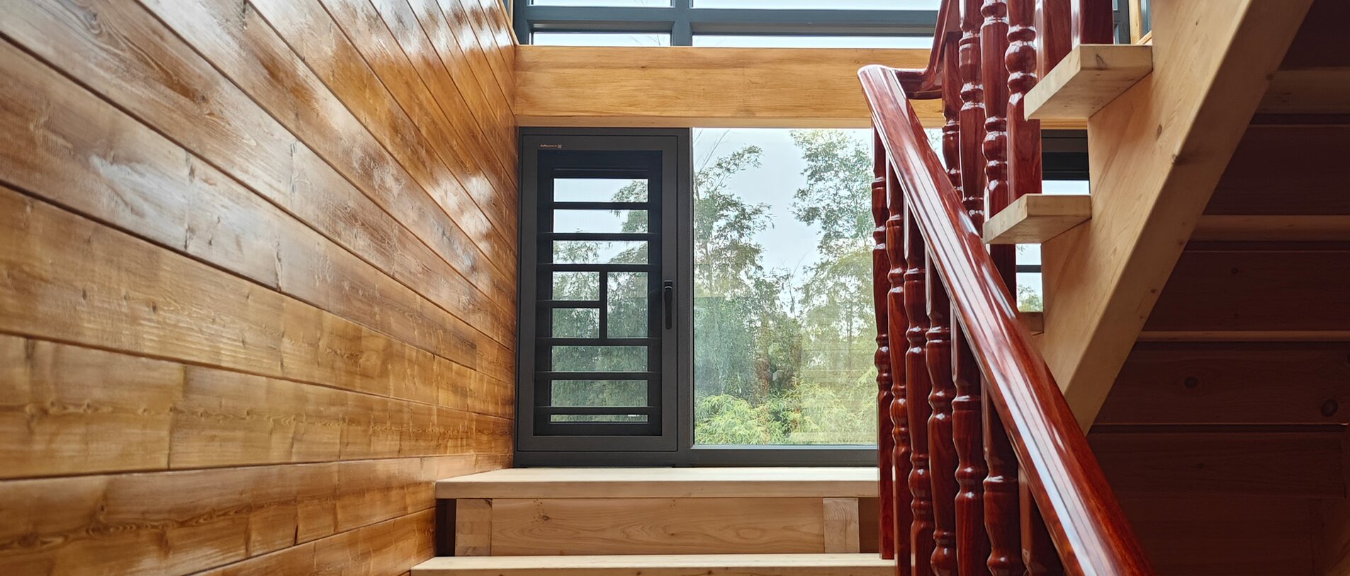 Treppenhaus in dunklem Holz mit großen Glasflächen nach draußen, realisiert mit LIGNOLOC® Holznägel von BECK