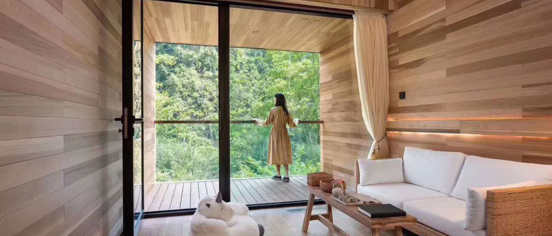 Bright living room with wooden interior and large glass front, offering a view of surrounding greenery