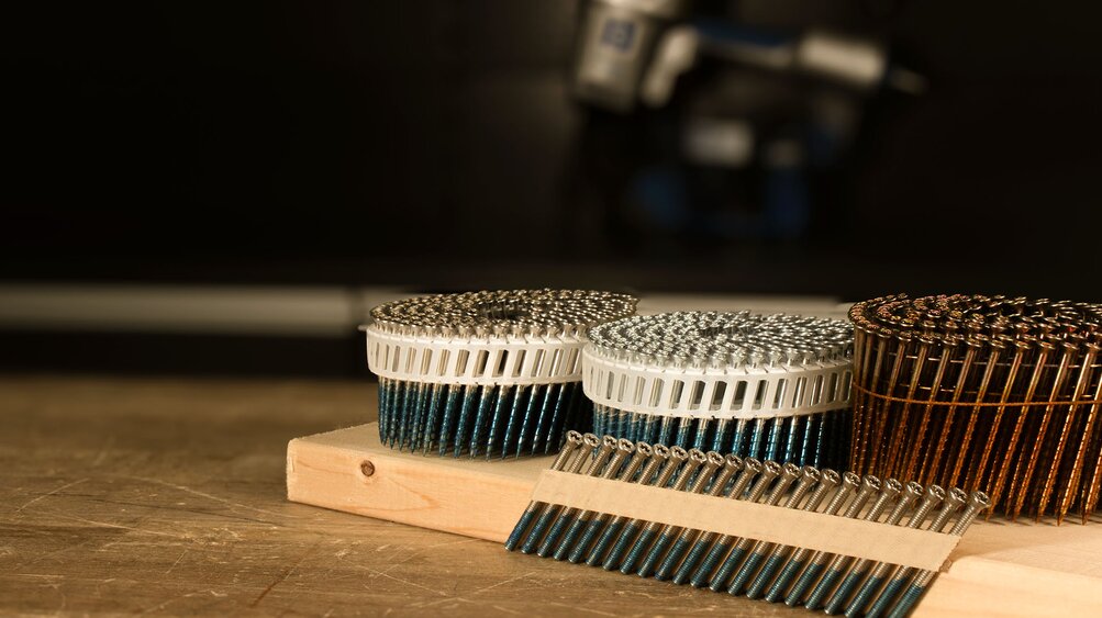 SCRAIL® nail screw fasteners and FASCO® pneumatic nailers by BECK SCRAIL® nail screw fasteners by BECK on a wooden workbench, FASCO® pneumatic nailers by BECK in the background.